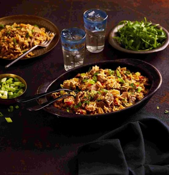 A serving dish of beef jambalaya on a table with accompanying salad