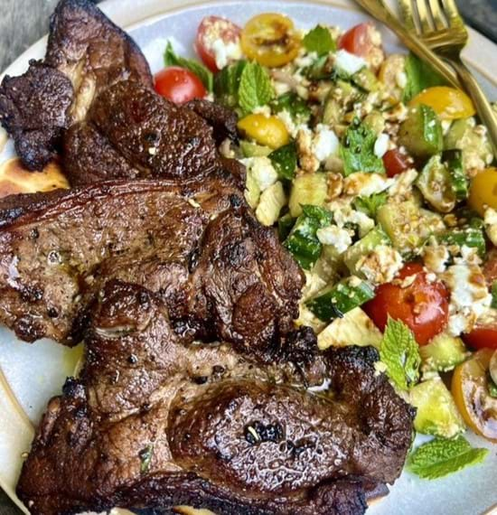 Mediterranean garlic lamb served with feta salad on a white plate.